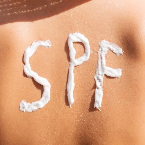 Yound girl has SPF written on her back with cream while sitting at a beach.